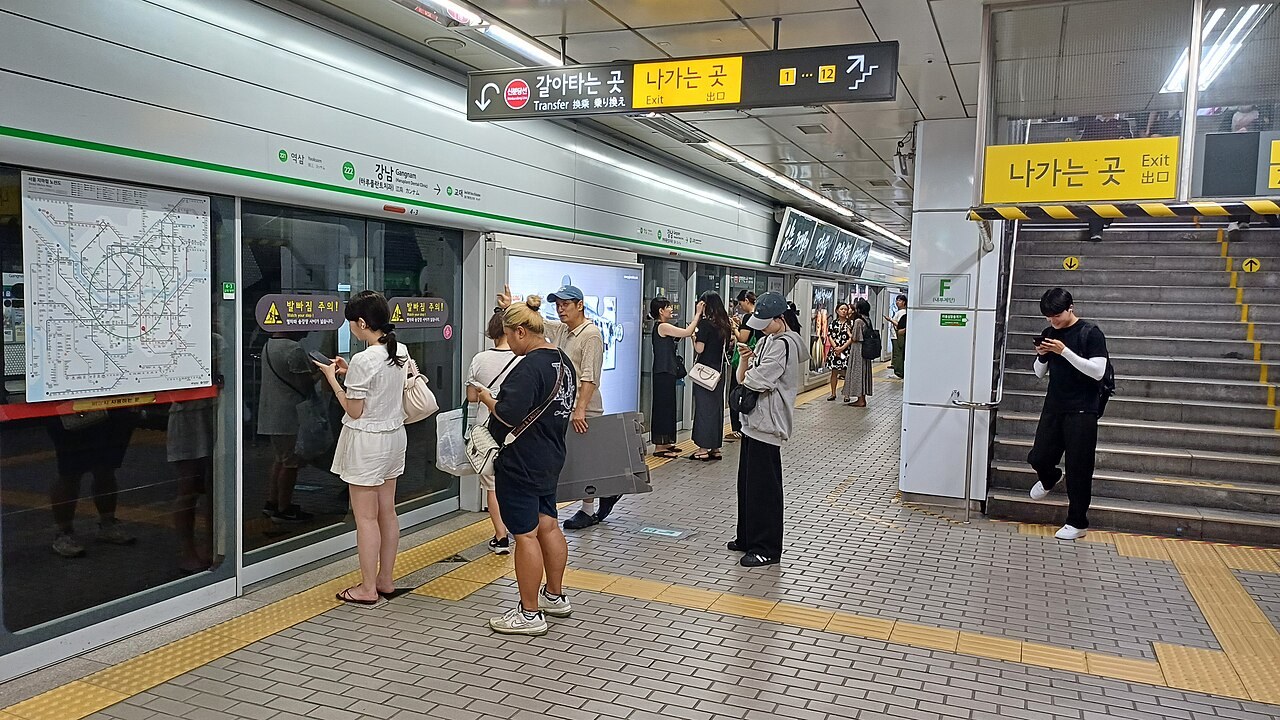 서울 지하철 2호선 강남역 승강장 안전문과 다국어 출구 안내 옆에서 기다리는 승객들